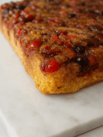 A close-up of a Cranberry Upside Down Cake featuring caramelized fruit and a golden brown base, resting on a white marble surface.