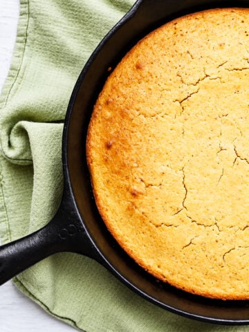 Golden brown grandmother's buttermilk cornbread in a black cast iron skillet resting on a green cloth.
