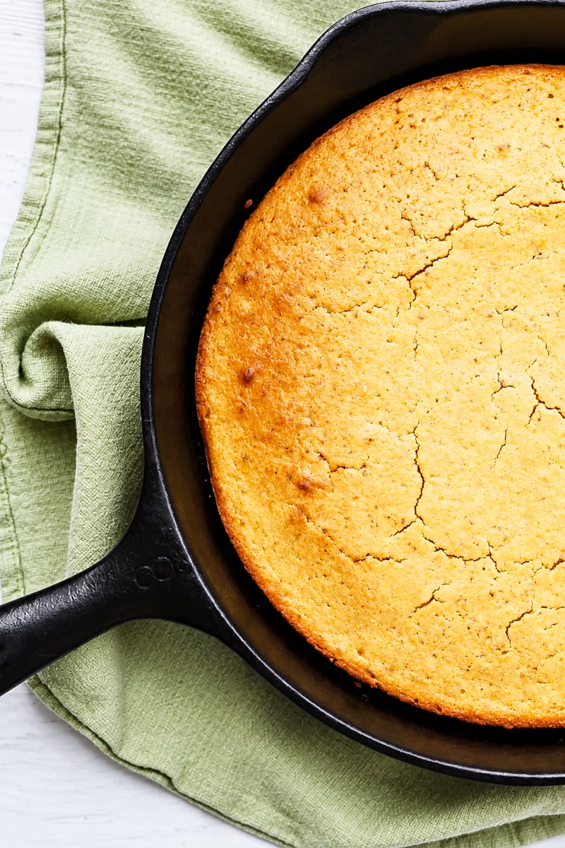 Golden brown grandmother's buttermilk cornbread in a black cast iron skillet resting on a green cloth.