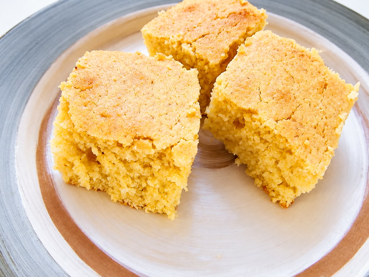 Three square pieces of grandmother’s buttermilk cornbread on a ceramic plate.