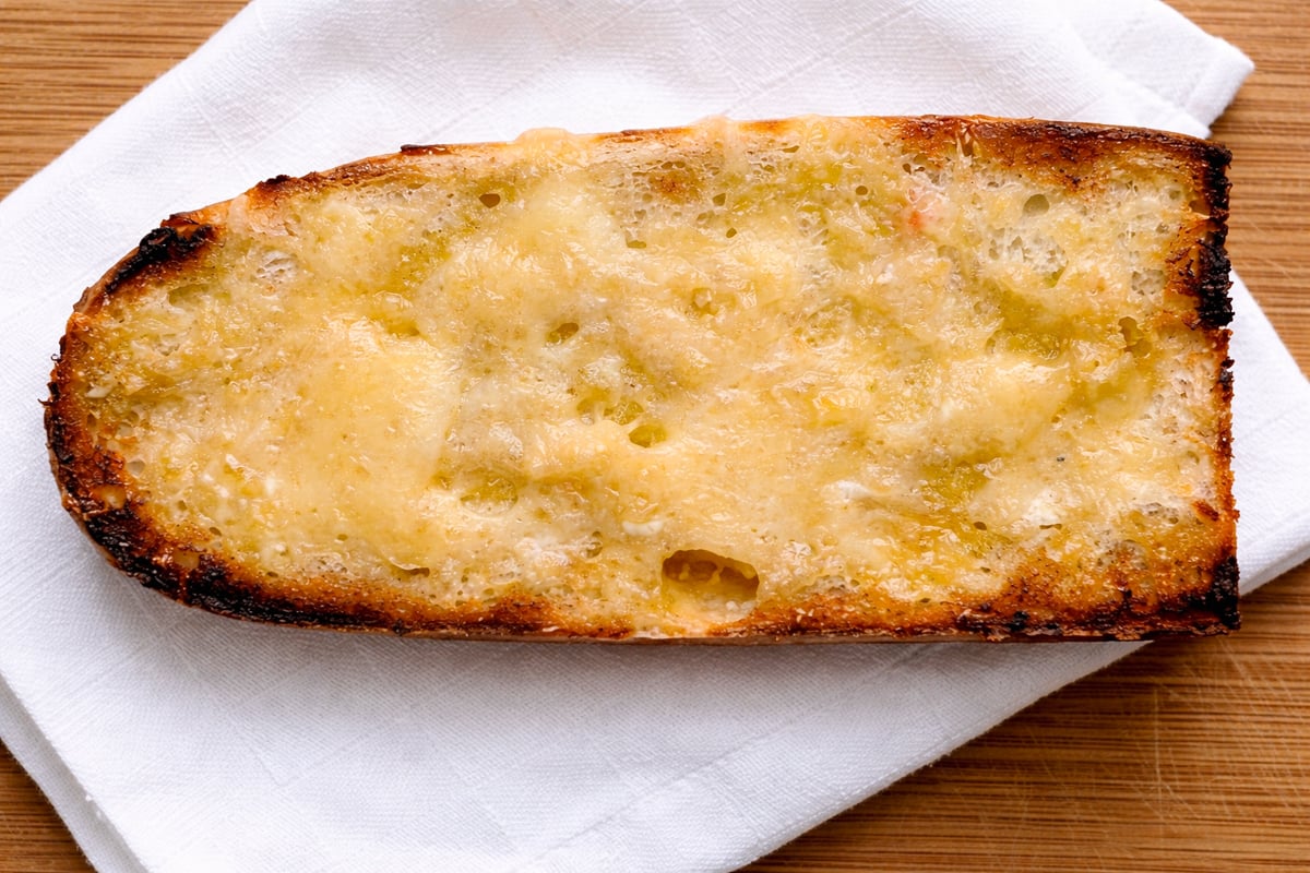 A toasted slice of bread topped with melted cheese, reminiscent of the perfect pairing for Zuppa di Fagioli—Italian Bean Soup—rests on a folded white napkin on a wooden surface.