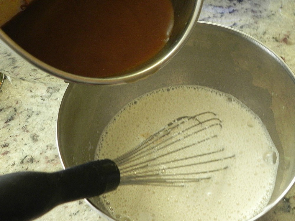 overhead image of brown sugar mixture pouring into a whipped egg mixture in a metal bowl