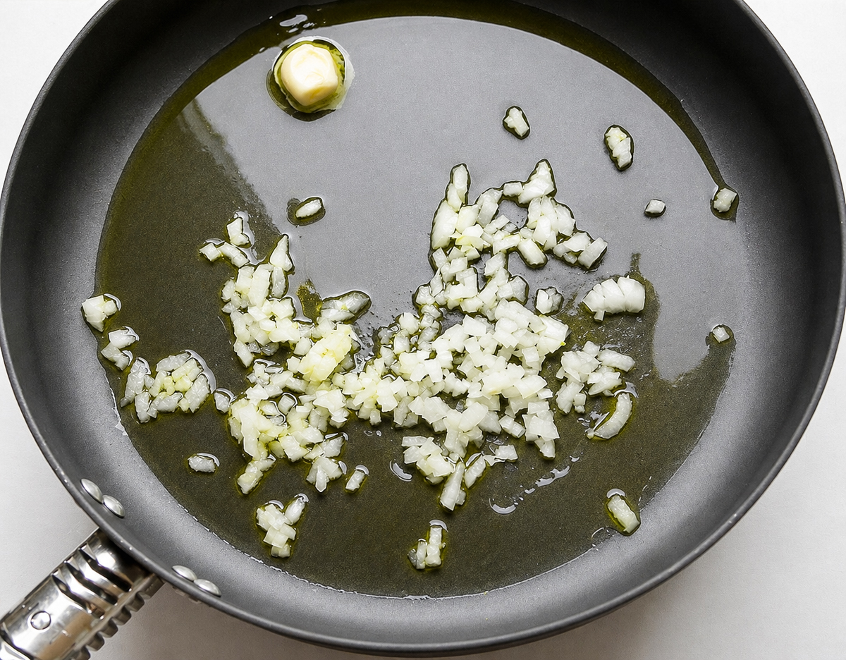 Chopped onions and a clove of garlic sizzle in olive oil in a black frying pan-the perfect base for Farfalle con Broccoli Rapini.
