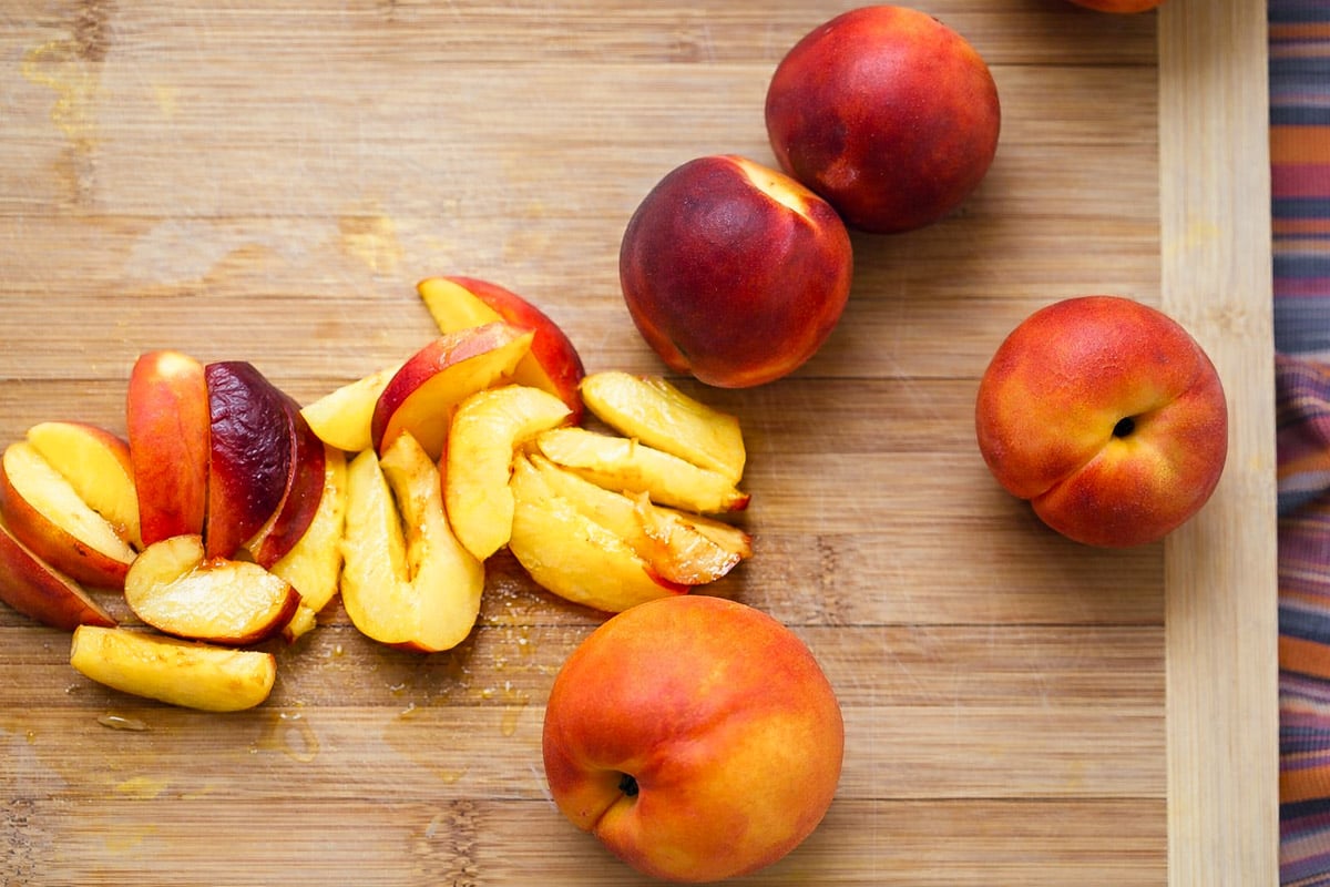 Sliced and whole nectarines are arranged on a wooden cutting board, ready to inspire your next Upside-Down Buttermilk Peach Cake. A colorful striped cloth adds charm at the edge of the scene.
