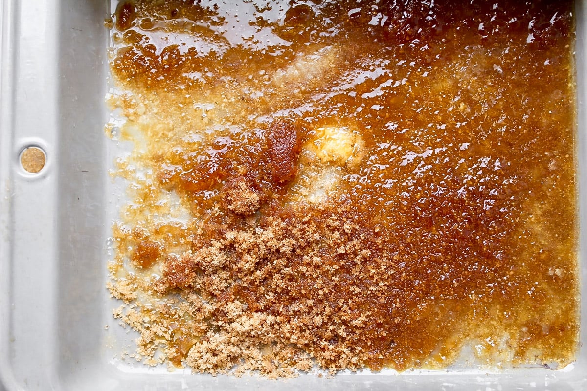 A metal baking pan with melted butter, coarse brown sugar, and light brown sugar partially mixed together creates a marbled, glossy base for an Upside-Down Buttermilk Peach Cake.