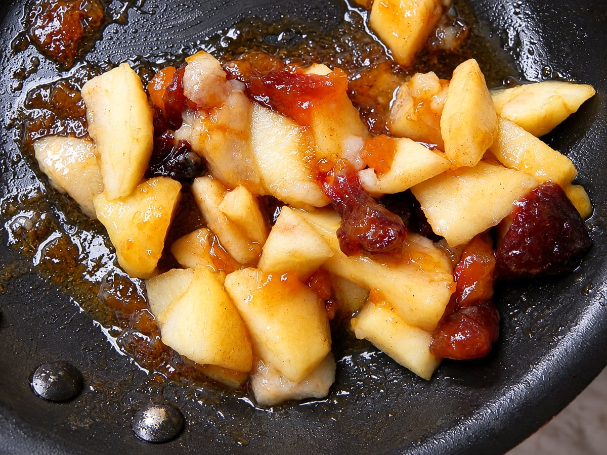 Chopped apples and dried fruit cooking in a pan with a syrupy glaze for an Autumn Crostata.