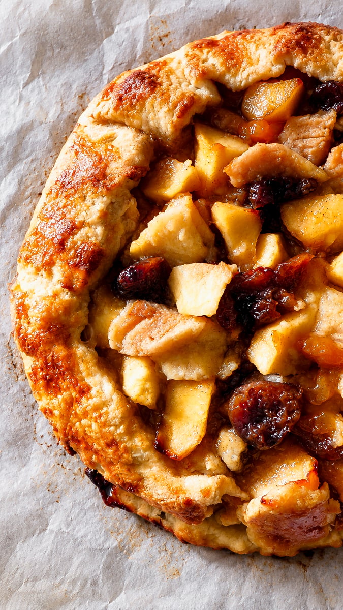 A rustic Autumn Crostata with a golden-brown crust, filled with sliced apples and dark fruit on parchment paper.