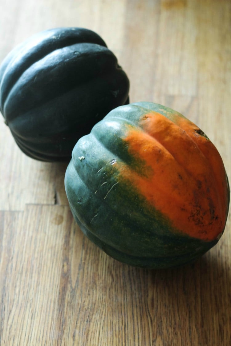 Image of two whole acorn squash on wood surface.