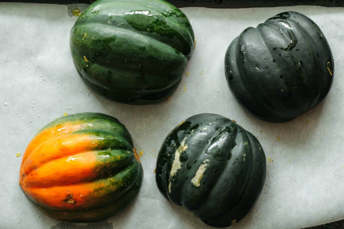 Overhead image of two acorn squash cut in half on parchment paper.