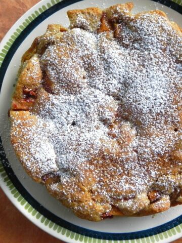 A homemade torta rustica dusted with powdered sugar sits on a patterned plate, placed on an orange surface. The words torta rustica appear in white and green text on the left side of the image.
