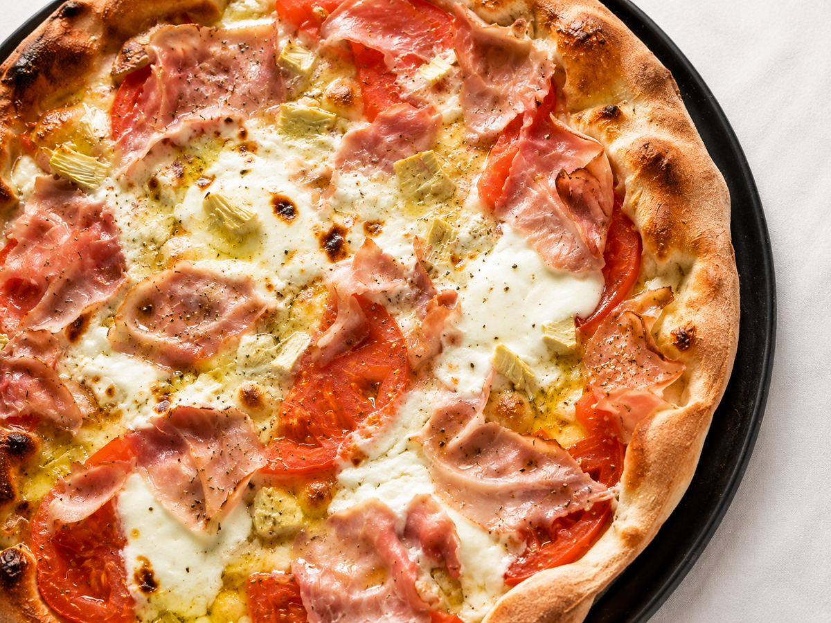 Close up of melted brie chunks and prosciutto cotto on a crispy homemade pizza crust