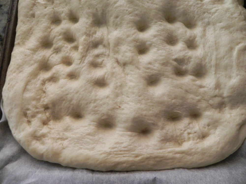 overhead image of dimpled focaccia dough in parchment lined pan