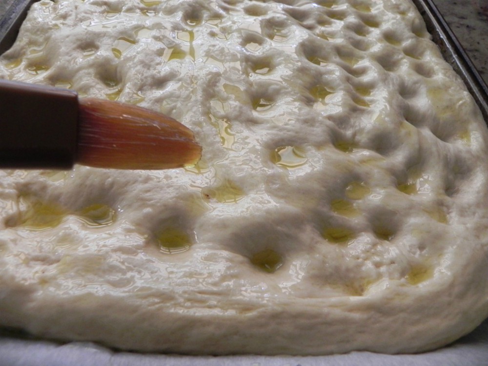 overhead image of brushing olive oil in dimples of dough