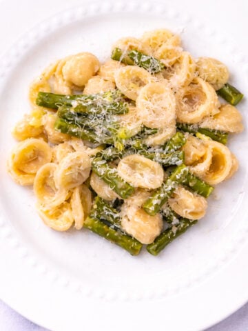 A white plate with orecchiette pasta, asparagus pieces, and a light creamy sauce, topped with grated cheese.