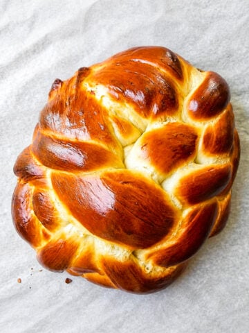 Golden braided honey challah bread on a parchment lined baking sheet