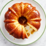 A glazed bundt cake with a slice removed, displayed on a white plate with a green rim.