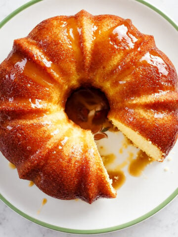 A glazed bundt cake with a slice removed, displayed on a white plate with a green rim.