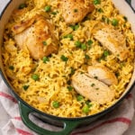 A green Dutch oven filled with yellow rice, green peas, and browned chicken pieces, garnished with chopped parsley, sits on a beige surface with a red-striped cloth-this is a Very Easy One Pot Chicken and Rice meal.