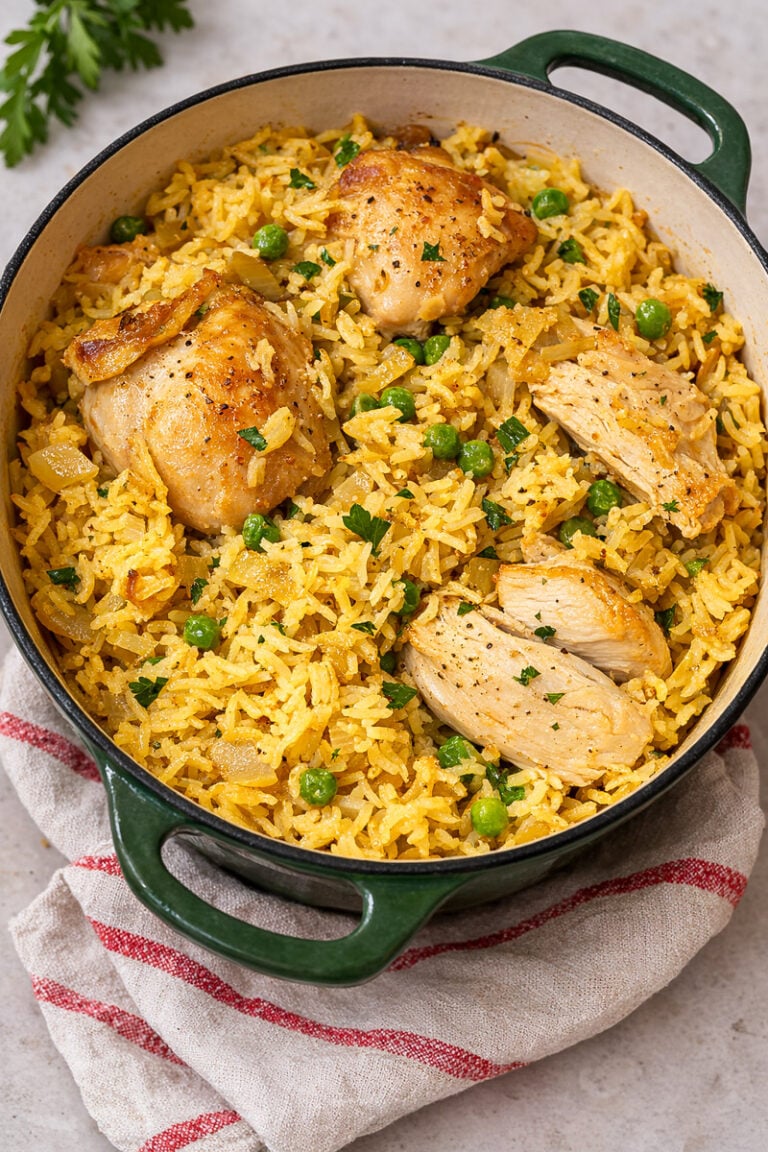 A green Dutch oven filled with yellow rice, green peas, and browned chicken pieces, garnished with chopped parsley, sits on a beige surface with a red-striped cloth—this is a Very Easy One Pot Chicken and Rice meal.