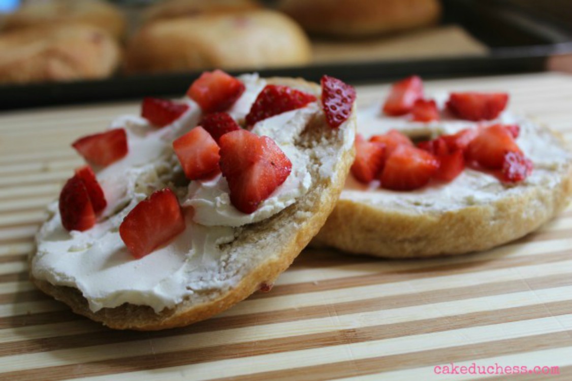 overhead image of bagel with cream cheese and strawberry chunks on wooden board