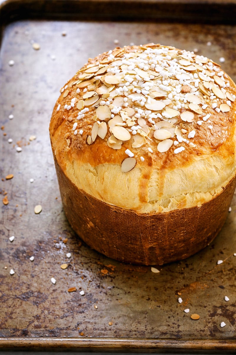 A round loaf of golden-brown Sicilian Orange Sweet Bread sits on a baking sheet, topped with sliced almonds and pearl sugar.
