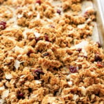 A close-up of super easy cranberry coconut granola on a baking sheet, featuring oats, dried cranberries, coconut flakes, and seeds, golden brown and freshly baked.