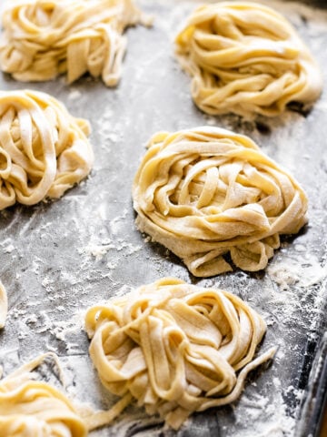 Freshly made nests of homemade fettuccine pasta rest on a floured metal baking sheet, ready to be cooked.