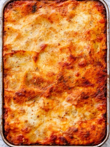 A rectangular baking dish filled with golden-brown, baked lasagna bolognese, its cheesy, bubbling top layer and patches of tomato sauce reveal the irresistible appeal of an authentic lasagna bolognese recipe.