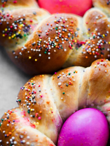 Two braided bread rings topped with colorful sprinkles, each holding a bright pink egg in the center-classic Italian Easter bread, typically enjoyed during festive celebrations like Easter.