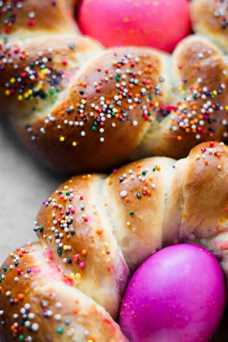 Two braided bread rings topped with colorful sprinkles, each holding a bright pink egg in the center—classic Italian Easter bread, typically enjoyed during festive celebrations like Easter.