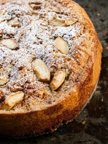 Italian vegan apple cake dusted with powdered sugar on a white cake stand