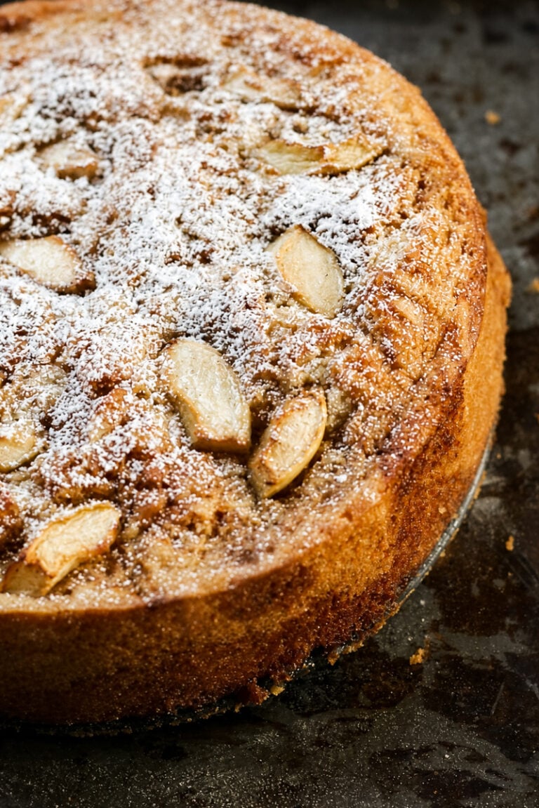 Italian vegan apple cake dusted with powdered sugar on a white cake stand