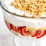 A glass trifle dish filled with layers of sliced strawberries, creamy pudding, whipped cream, and topped with crumbled amaretti cookies creates a delightful strawberry and amaretti cookie trifle.