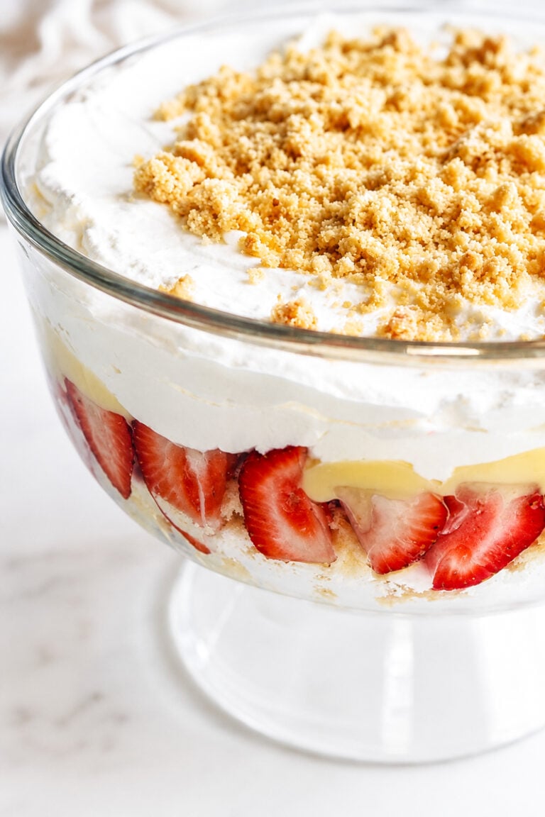 A glass trifle dish filled with layers of sliced strawberries, creamy pudding, whipped cream, and topped with crumbled amaretti cookies creates a delightful strawberry and amaretti cookie trifle.
