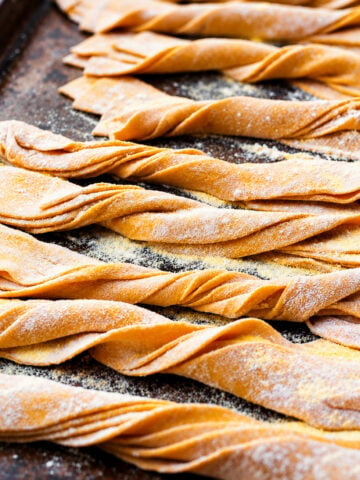 Several rows of twisted homemade pumpkin pappardelle dusted with flour on a baking sheet.