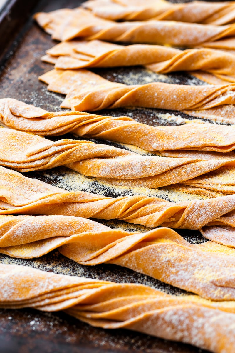 Several rows of twisted homemade pumpkin pappardelle dusted with flour on a baking sheet.
