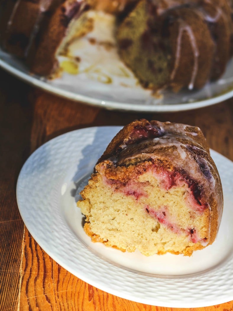 close up image of slice of glazed strawberry cake from scratch on plate.