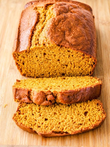 A loaf of sliced pumpkin bread on a wooden cutting board.