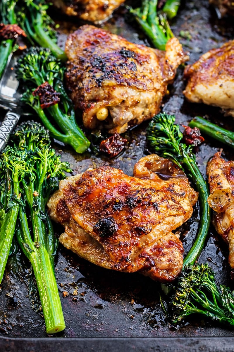 Sheet Pan Honey Balsamic Chicken Thighs with Broccolini is no-fuss and just delicious! The most irresistible honey balsamic sauce and the best thing is hardly any clean up! #chicken #sheetpan #glutenfree #easydinner Sheet Pan Honey Balsamic Chicken Thighs with Broccolini are roasted on a dark baking sheet, featuring caramelized edges and vibrant greens. A rustic, appetizing meal, with a fork partially visible at the side.