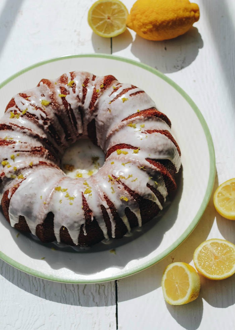 lemon curd cake on white plate surrounded by lemons