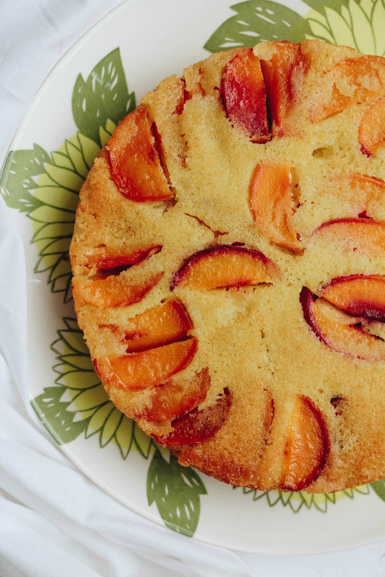 overhead image of vegan peach polenta cake on a serving dish.