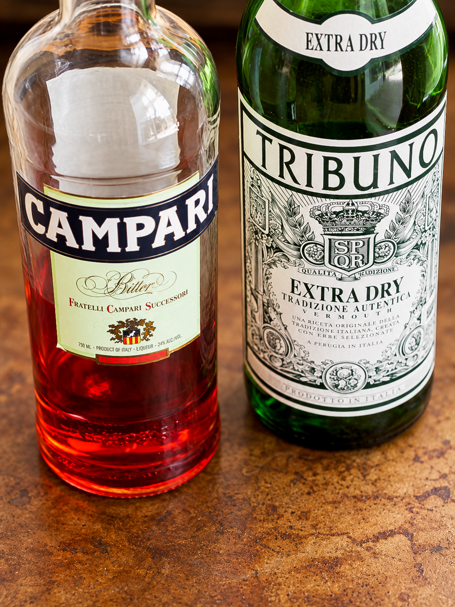A bottle of red Campari liqueur next to a bottle of Tribuno Extra Dry vermouth, often used in recipes for an Italian cranberry sauce.