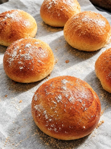 Six golden-brown savory corn rolls sprinkled with flour on parchment paper.