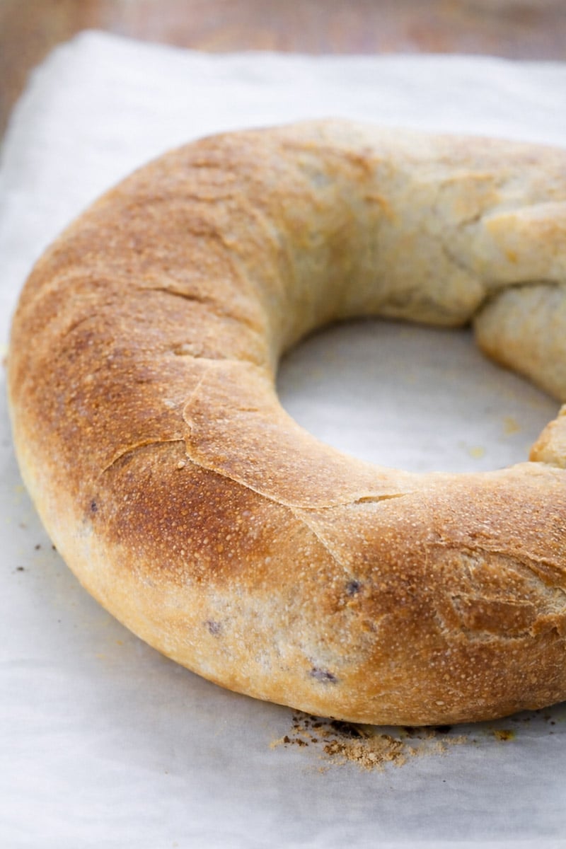 A golden-brown, rustic Casatiello—a traditional ring-shaped loaf of bread—rests on a sheet of white parchment paper.