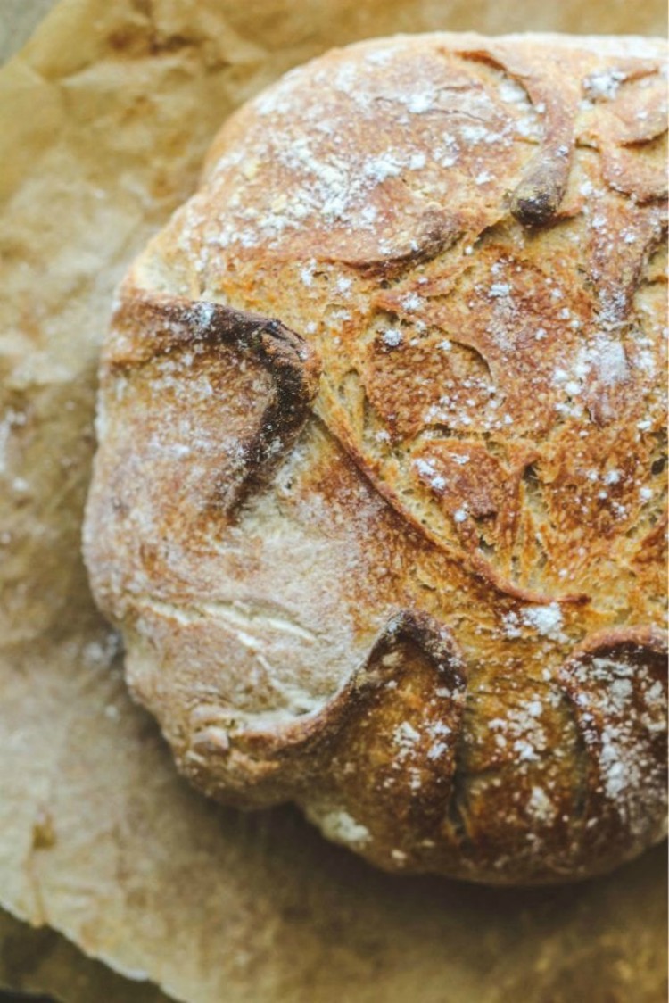 overhead image of crusty round loaf of bread on parchment paper