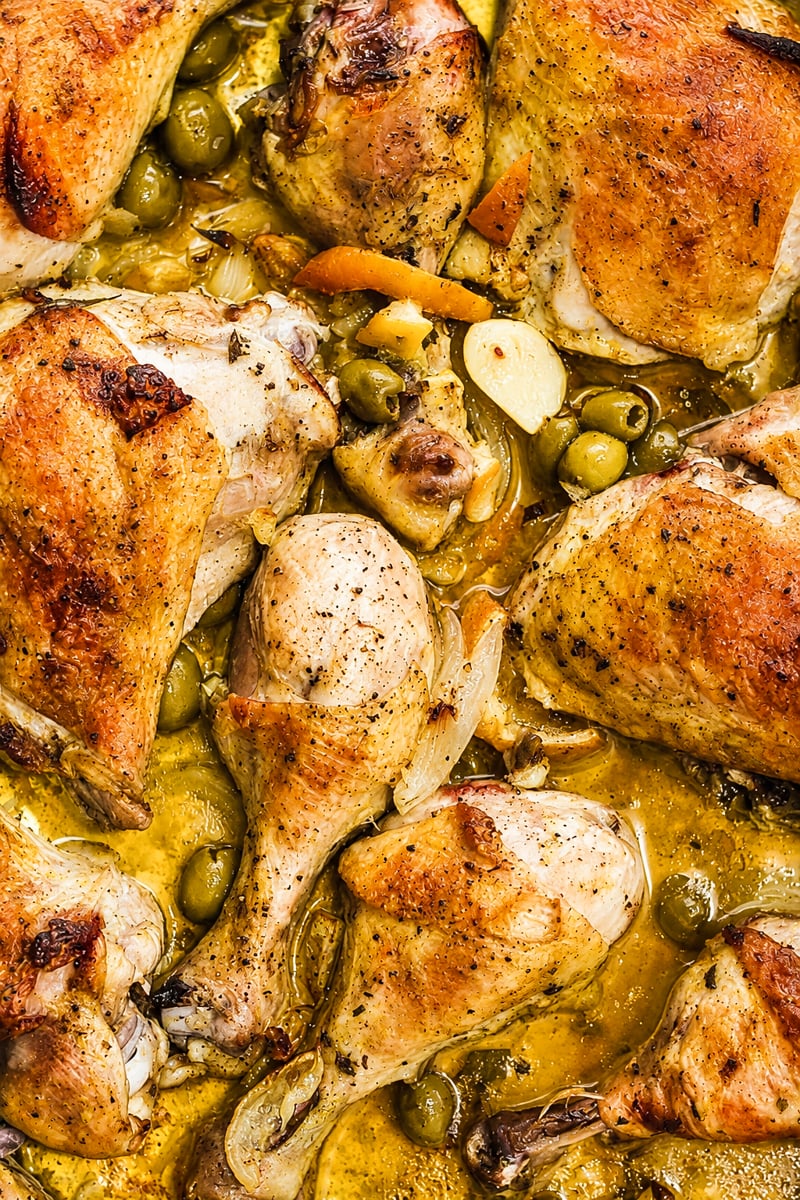 Roasted chicken pieces with golden skin, surrounded by green olives, sliced garlic, and herbs in a savory sauce-a classic Chicken with Preserved Meyer Lemons and Olives for unforgettable flavor.
