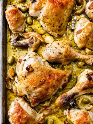 Roasted chicken pieces with golden brown skin on a baking sheet, surrounded by green olives, sliced onions, and a savory sauce-this Chicken with Preserved Meyer Lemons and Olives brings vibrant citrus notes that perfectly complement the rich flavors of the dish.