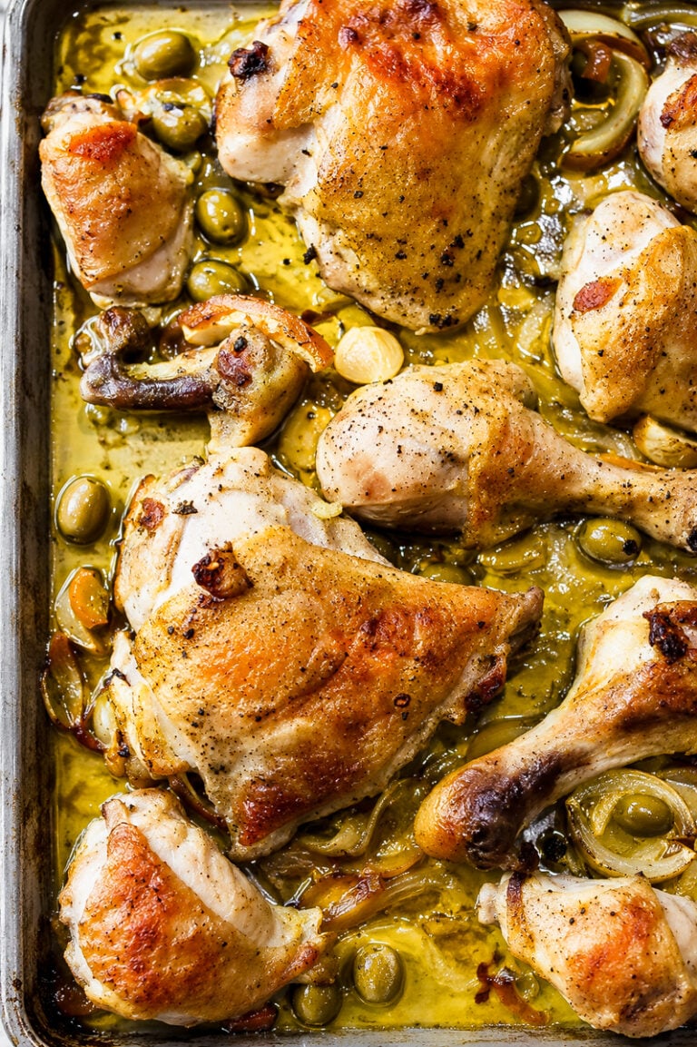 Roasted chicken pieces with golden brown skin on a baking sheet, surrounded by green olives, sliced onions, and a savory sauce—this Chicken with Preserved Meyer Lemons and Olives brings vibrant citrus notes that perfectly complement the rich flavors of the dish.