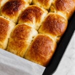 Golden brown, freshly baked Barley Malt Pull-Apart Loaves in a black baking pan lined with parchment paper, resting on a light marble surface.