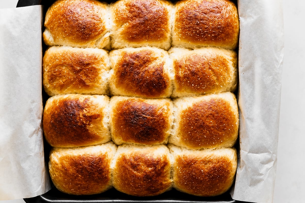 A baking pan lined with parchment paper holds twelve golden-brown Barley Malt Pull-Apart Loaves, freshly baked and arranged in a 3x4 grid.